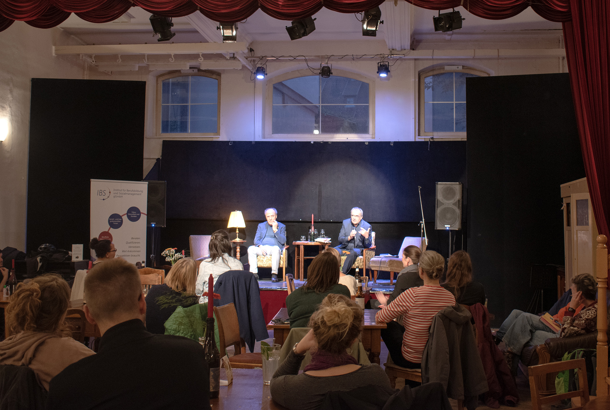 Die beiden Autoren sitzen auf dem Podium des Cafe Nerly und stellen ihr Buch vor.